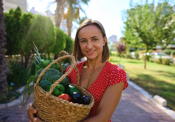 Woman holding wooden box full of fresh raw vegetables. Basket with fruits and vegetable with peppers, tomatoes, broccoli, banana peaches, grape in the hands. High quality photo
