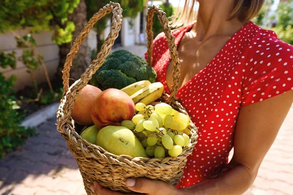 Woman holding wooden box full of fresh raw vegetables. Basket with fruits and vegetable with peppers, tomatoes, broccoli, banana peaches, grape in the hands. High quality photo