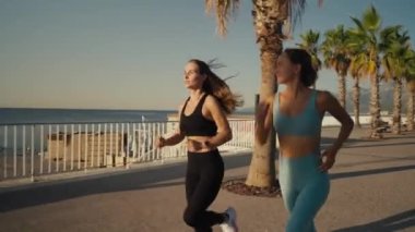 Two beautiful girls jogging at sunset or sunrise on beach. Young caucasian women running together. Brunette and blonde are smiling. Feeling of freedom while running. Concept of cardio.