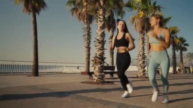 Two beautiful girls jogging at sunset or sunrise on beach. Young caucasian women running together. Brunette and blonde are smiling. Feeling of freedom while running. Concept of cardio.
