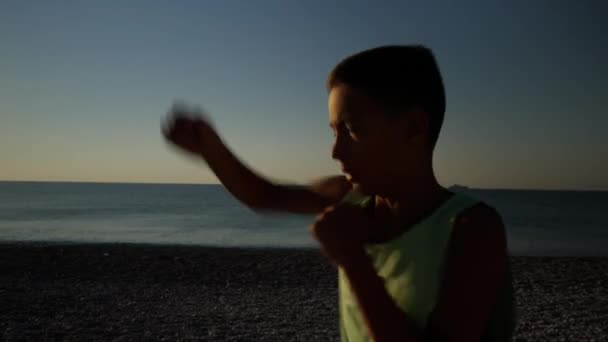 日の出の間にビーチで若い男性ボクサーや空手の戦闘機の訓練 午前中にシャドウボクシングをやっている少年のシルエットのショット 高品質4K映像 — ストック動画