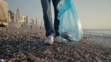 Plajda terk edilmiş plastik şişeleri toplayan genç bir kadın. Kadınlar sahilde çöp topluyor.