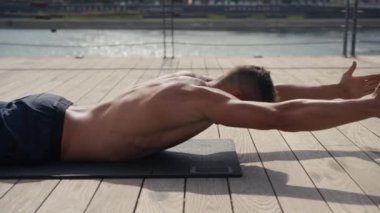 Beyaz bir adam Superman Back Extensions 'ı siyah bir paspasın üzerinde yapıyor. Isome egzersizi. Açık havada sırt kaslarını çalıştırıp çalıştırıyor..