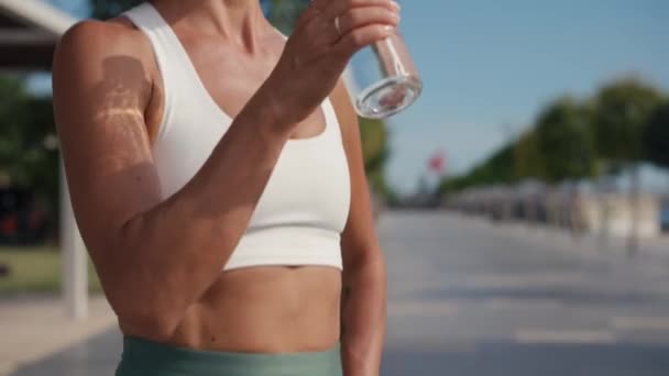 若い運動選手の女性は晴れた日に水を飲む 女性は雲の動きが遅い青空に対してガラス瓶から水を飲む 高品質4K映像 — ストック動画