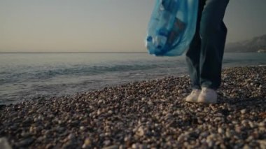 Plajda terk edilmiş plastik şişeleri toplayan genç bir kadın. Kadınlar sahilde çöp topluyor.