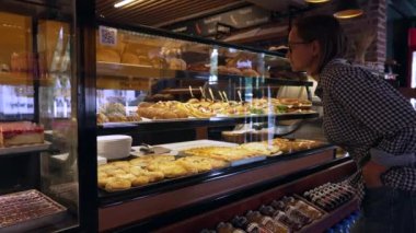 Genç kadın pastayı seçiyor. Buzdolabında çeşitli tatlılar var. Müşteri pastaya bakar ve bir seçim yapar. Yüksek kalite 4k görüntü