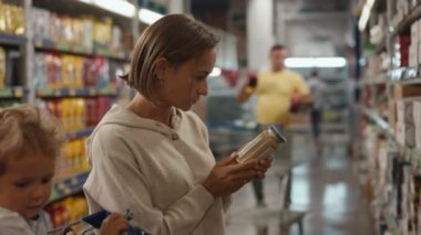 Alıcının ürünleri süpermarketin raflarından seçtiği kız. Alıcı konserve yiyecek kavanozunun ürününü inceliyor. Bir el, bir mağaza rafından bir ürün alıyor.. 