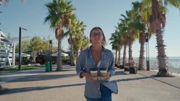 Молодая Белая Женщина Двумя Чашками Кофе Улыбающаяся Идущая Берегу Моря — стоковое видео
