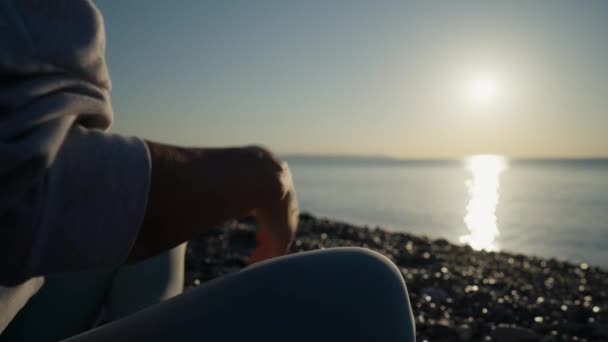 年轻的穿着运动服的高加索女人通过在平静的海面附近的海滩上练习瑜伽 手拉手 陀螺泥浆和莲花姿势来放松身体 日出背景 慢动作高质量的4K镜头 — 图库视频影像