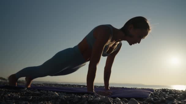年轻的高加索女人练习瑜伽 年轻健康的女子日出时在海滩上练习瑜伽 — 图库视频影像