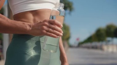 Genç atletik kadın güneşli bir günde su içer. Bayan cam şişeden mavi gökyüzüne doğru yavaş çekimde su içiyor. Yüksek kalite 4k görüntü