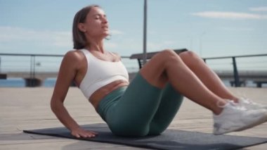 Sportif formda genç bir kadın bisiklet çatırdatma egzersizi yapıyor, tahta zeminde yatıyor, güçlü bir sporcu kadın aktif giysi giyiyor, karın kaslarını çalıştırıyor..