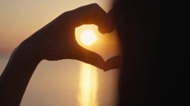 Gün batımı siluetiyle kalp şeklinde eller.