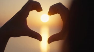 Gün batımı siluetiyle kalp şeklinde eller.