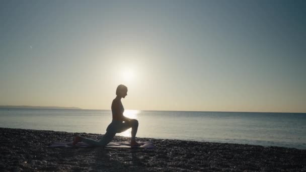 年轻的高加索女人练习瑜伽 年轻健康的女子日出时在海滩上练习瑜伽 — 图库视频影像
