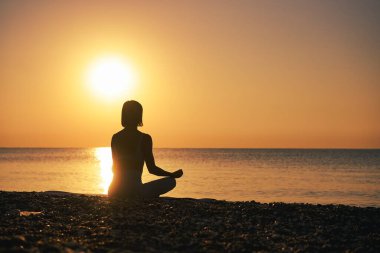 Siluet genç kadın gün batımında plajda yoga yapıyor. Yüksek kalite fotoğraf