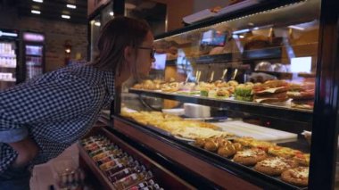 Genç kadın pastayı seçiyor. Buzdolabında çeşitli tatlılar var. Müşteri pastaya bakar ve bir seçim yapar. Yüksek kalite 4k görüntü