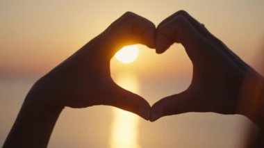 Gün batımı siluetiyle kalp şeklinde eller.