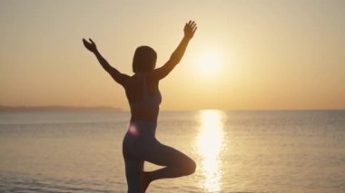 Siluet Kadın, yaz tatili plaj mutluluğu ve rahatlama ile meditasyona yoga pozu veriyor. Yogayla sakin kadın egzersizleri okyanus sahilinde altın günbatımında meditasyon yapar. Ruh Sağlığı
