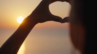 Gün batımı siluetiyle kalp şeklinde eller.