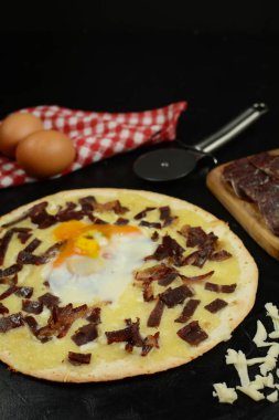 Siyah zemin üzerinde taze pizza ve malzemeler.