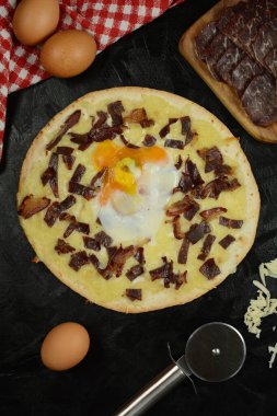 Siyah zemin üzerinde taze pizza ve malzemeler.