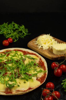 Siyah zemin üzerinde taze pizza ve malzemeler.