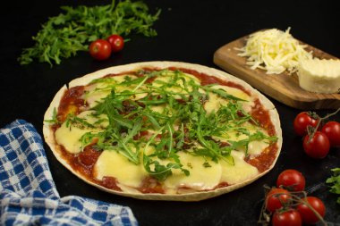 Siyah zemin üzerinde taze pizza ve malzemeler.