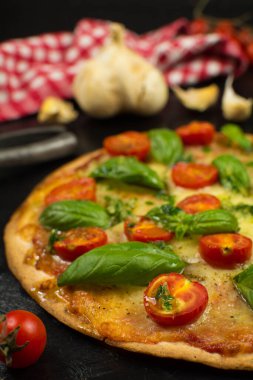 Siyah zemin üzerinde taze pizza ve malzemeler.