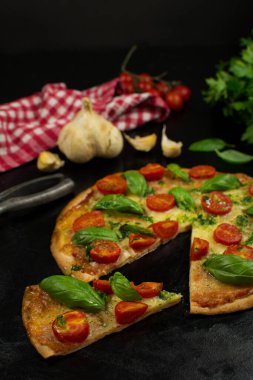 Siyah zemin üzerinde taze pizza ve malzemeler.