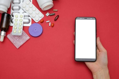 Kırmızı arka planda ilaç ve akıllı telefon var.