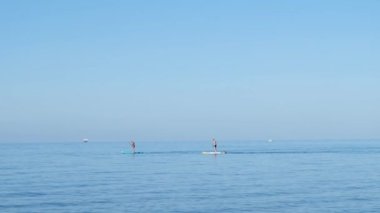 Mavi denizde ayakta duran iki adam, çok güzel ve sakin bir manzara.