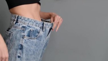 İnce beli olan genç fitness kadını büyük pantolonları dener ve kameraya nasıl kilo verileceğini gösterir. Atletik kız diyet ve egzersizden sonra kilo verdi