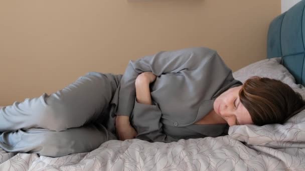 Στρεσαρισμένη νεαρή γυναίκα ξαπλωμένη στο κρεβάτι, αγκαλιάζει την κοιλιά, υποφέρει από στομαχόπονο ή πόνο στην έμμηνο ρύση. Γαστρίτιδα, κοιλιακή ή περίοδο έννοια του πόνου. — Αρχείο Βίντεο