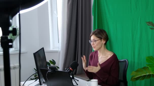ブロガー中年女性彼女のブログやソーシャルメディアのためのウェブカメラを介してビジネスビデオを撮影,緑の背景に自宅で. — ストック動画