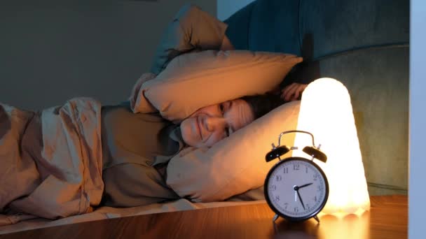 Unzufriedene junge Frau kann nicht schlafen, weil sich laute Geräusche, die Ohren mit Kissen im Bett bedecken, gestresst anfühlen. Menschen und Lebensstil-Konzept. — Stockvideo