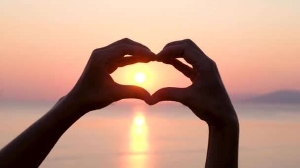 Mani a forma di cuore durante il tramonto sull'oceano o sul mare. Silhouette Close up — Video Stock