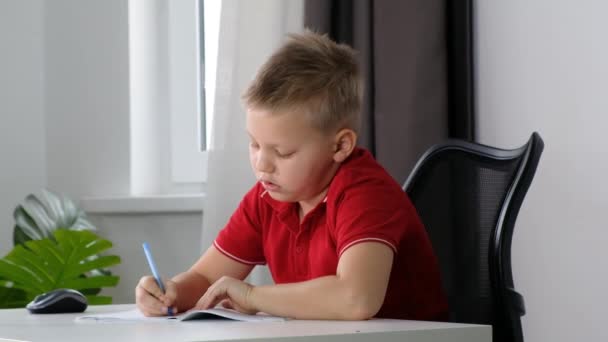 Το αγόρι Παιδί του σχολείου κάνει τα μαθήματά του στο σπίτι και αισθάνεται κουρασμένος, νυσταγμένος και βαριέται διαβάζοντας — Αρχείο Βίντεο