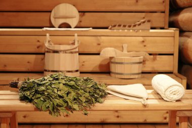 Tahta bir bankta huş süpürgesi ve Rus hamamının içinde geleneksel sauna aksesuarları.. 