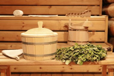 Tahta bir bankta huş süpürgesi ve Rus hamamının içinde geleneksel sauna aksesuarları.. 