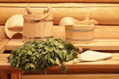 Geleneksel sauna aksesuarlarının arka planında, banyonun içindeki ahşap bankta kurumuş bir huş ağacı süpürgesi..