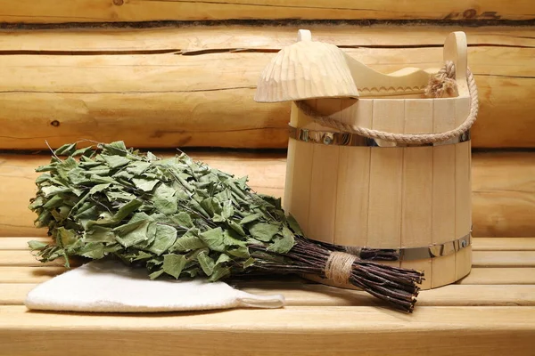 On a wooden bench in the bath a dry birch broom lies near other sauna accessories.