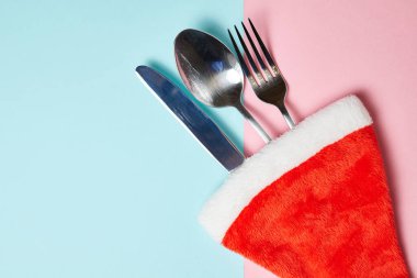 Noel Baba şapkasıyla bıçak, çatal ve kaşık pembe ve mavi arka planda fotokopi alanı ile