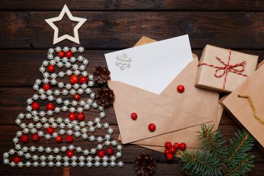 Noel ağacı boncuk ve mektuptan yapılmış bir zarf içinde ağaç dallarıyla ahşap arka planda yazılar olan mutlu noeller.