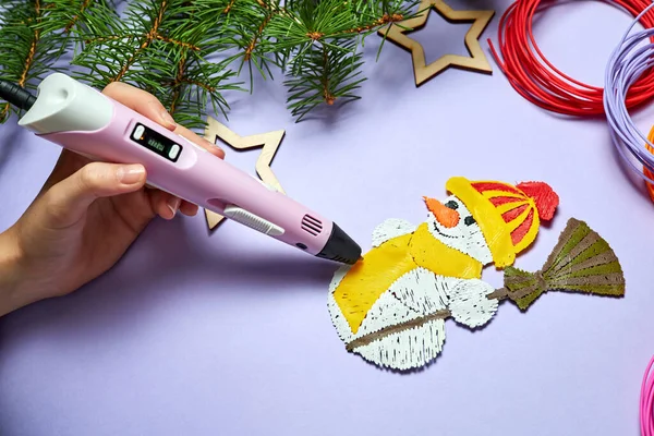 Bir kız mor arka planda 3 boyutlu kalem kullanarak kardan adam çiziyor.