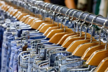 Elbise mağazasındaki askıda asılı duran çeşitli mavi kot pantolonlar. Yakın çekim, seçici odaklanma