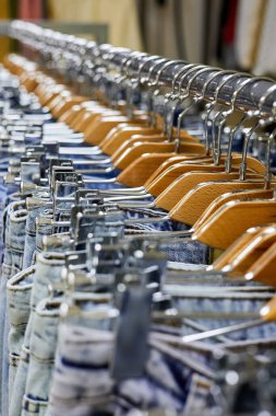 Elbise mağazasındaki askıda asılı duran çeşitli mavi kot pantolonlar. Yakın çekim, seçici odaklanma