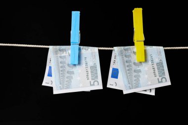 Çamaşır iğneleriyle tutturulmuş beş avroluk banknotlar, koyu arkaplanda çamaşır ipinde kurutuluyor