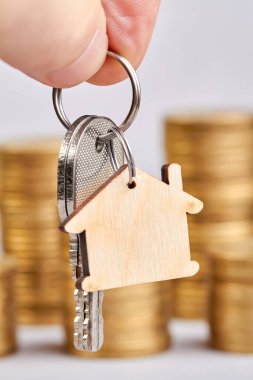 Bir adam yeni bir dairenin anahtarlarını para yığınlarının arkasında tutuyor.