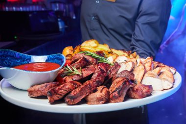 Garson bir tabak domuz eti ve fırında patates, domates ve sos ile tavuk kebabı tutuyor.